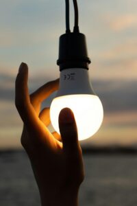 A hand holding a glowing light bulb against a twilight sky, symbolizing ideas and innovation.